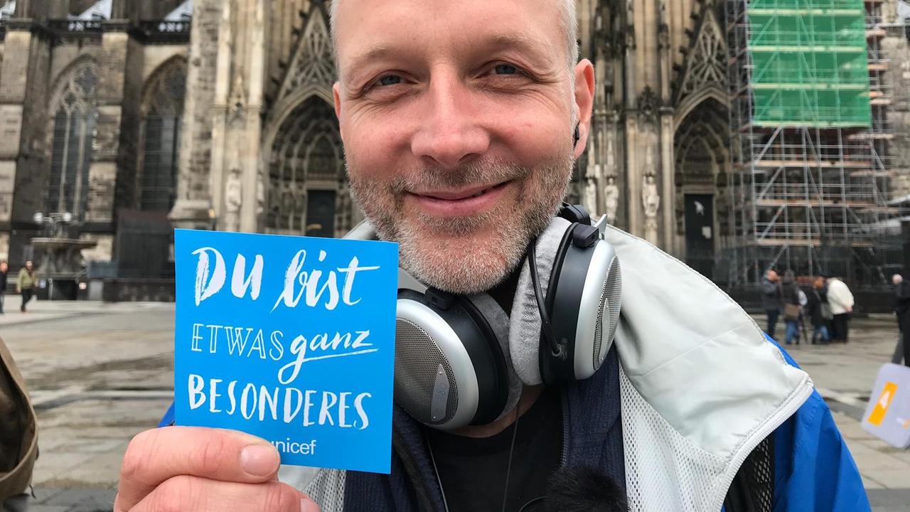 Unser Reporter vor dem Kölner Dom grinst in die Kamera und hält ein Schild hoch, auf dem "Du bist etwas ganz Besonderes" steht.