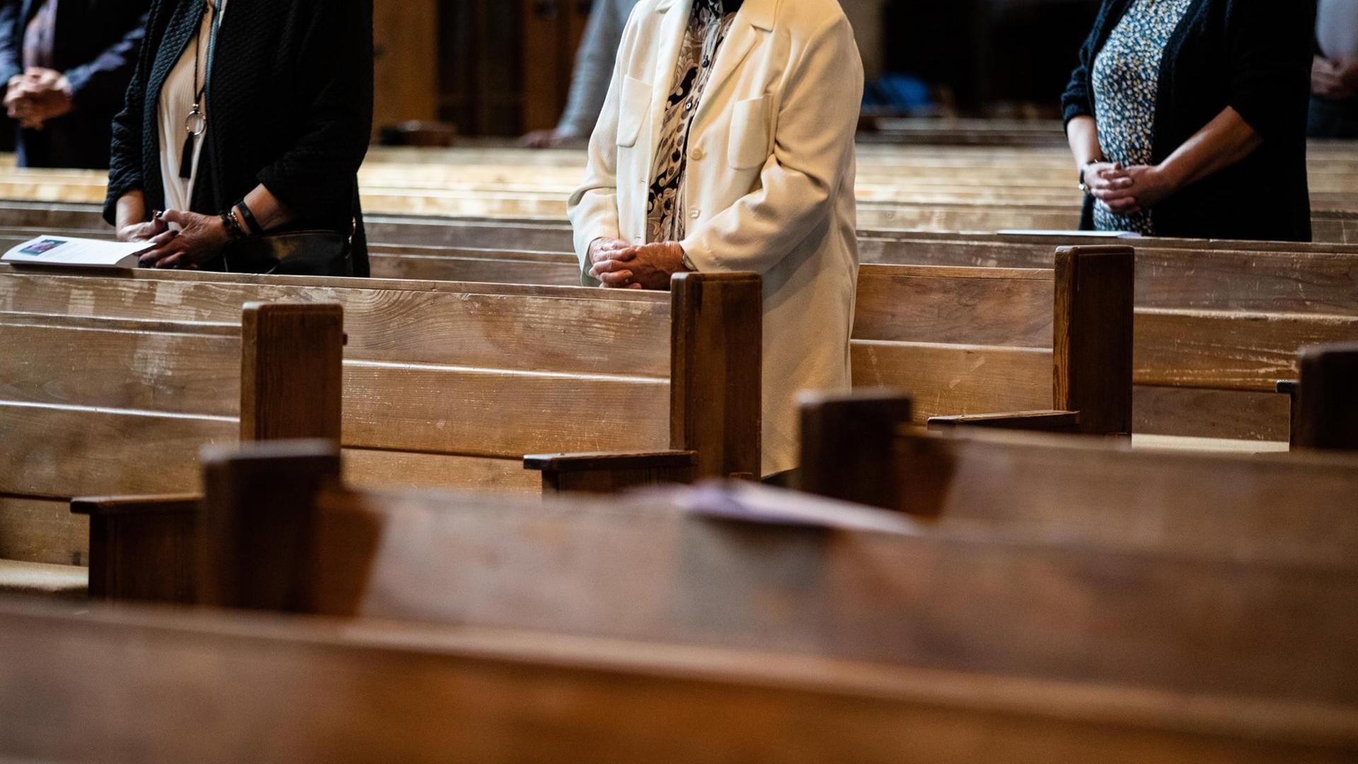 Kirchenbesucher mit gefalteten Händen zwischen Kirchenbänken Kirchenbesucher mit gefalteten Händen zwischen Kirchenbänken