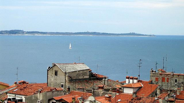 Blick auf die Bucht vom slowenischen Piran aus, dessen Häuser im Vordergrund zu sehen sind. Hinten ist die kroatische Küste der Halbinsel Istrien zu erkennen.
