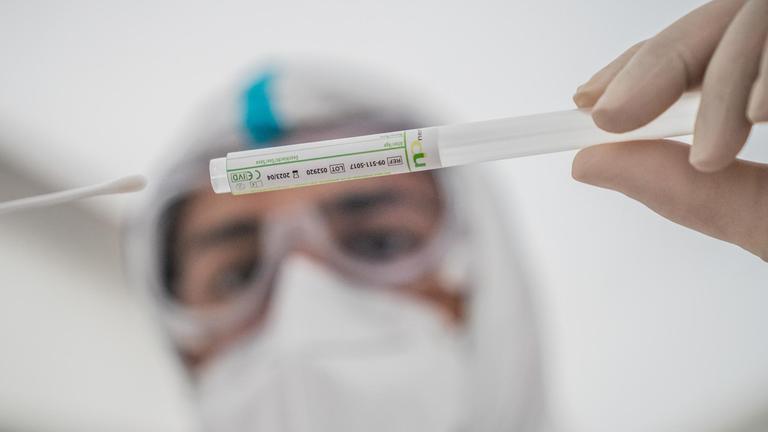 Ein Mitglied des medizinischen Personals steckt ein Wattestäbchen nach einem PCR-Abstrich zum Test auf COVID-19 in ein Röhrchen.
