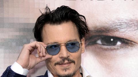 Hauptdarsteller Johnny Depp steht bei der Premiere von "Transcendence" in Westwood, Kalifornien, mit Sonnenbrille vor einem Filmplakat.