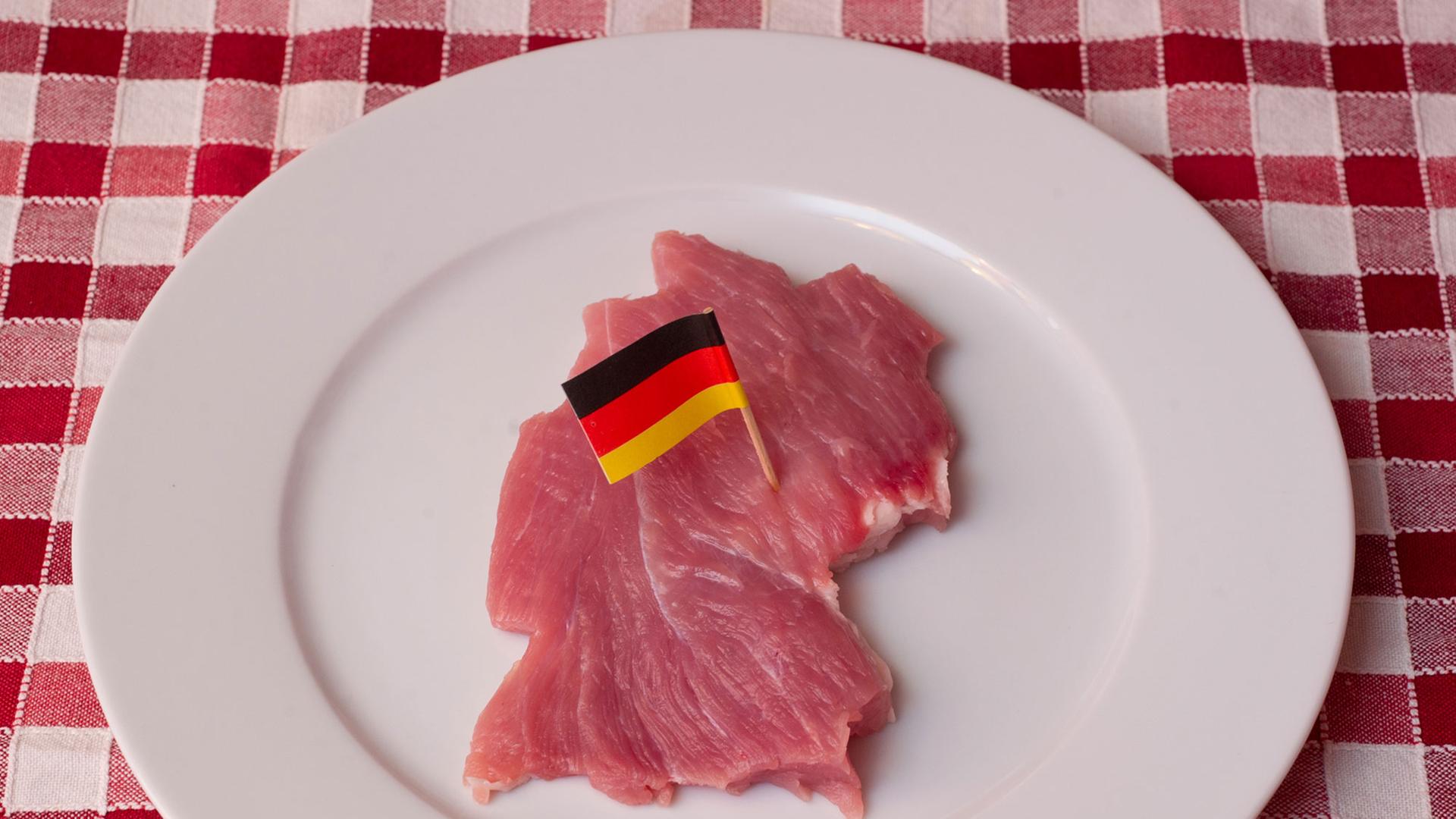 Ein Stück Schweinefleisch, geschnitten wie der Umriss von Deutschland und mit einer kleinen Deutschlandfahne Ein Stück Schweinefleisch, geschnitten wie der Umriss von Deutschland und mit einer kleinen Deutschlandfahne