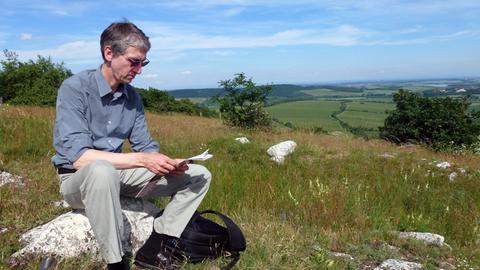 Der Komponist Hauke Harder sitzt in einer weiten Hügellandschaft auf einem Stein