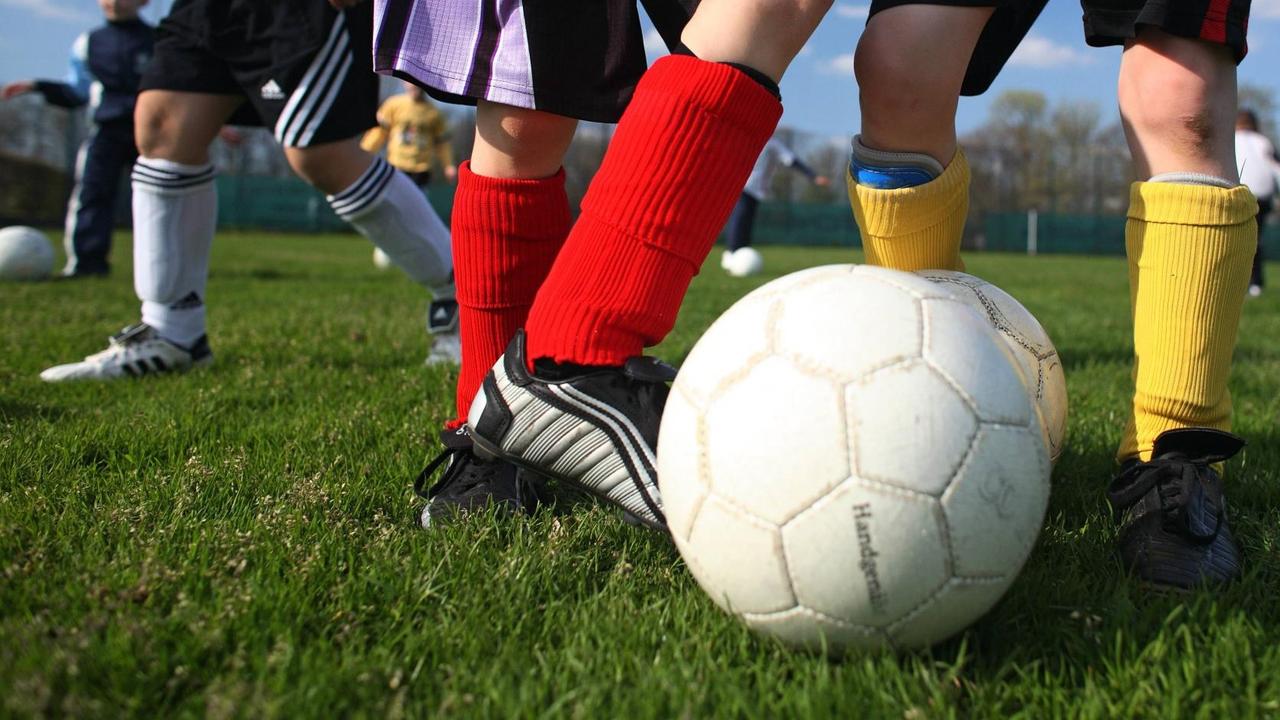 Die Sport-Schuhe und Beine von Kindern sind zu sehen. Sie spielen Fußball.