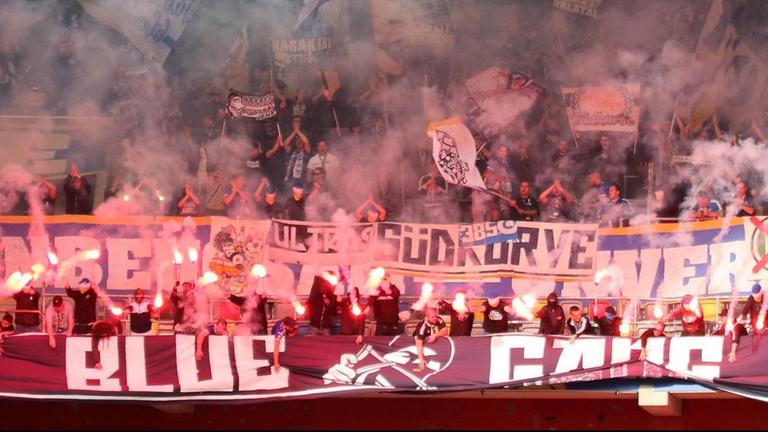 Bei einem Fußballspiel unterstützen Fans ihre Mannschaft auf den Rängen mit dem Abzünden von Bengalischen Feuern.