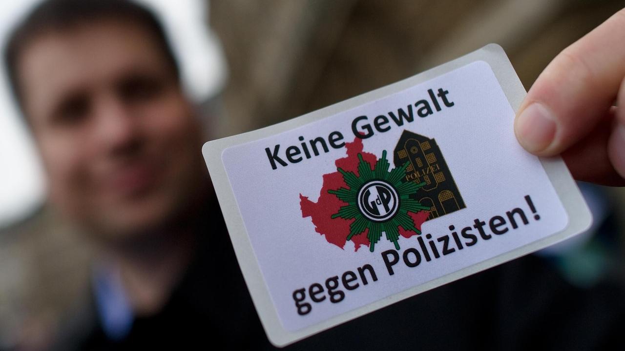 Ein Polizist hält einen Aufkleber hoch mit der Aufschrift "Keine Gewalt gegen Polizisten" Ein Polizist hält einen Aufkleber hoch mit der Aufschrift "Keine Gewalt gegen Polizisten"
