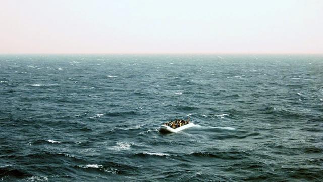 Ein Schlauchboot mit Flüchtlingen ist in der Entfernung im aufgewühlten Mittelmeer zu sehen