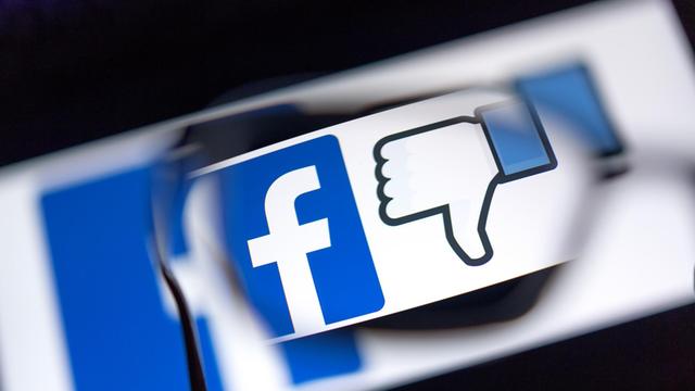 Das Logo des sozialen Netzwerks Facebook und das Zeichen für "Gefällt mir nicht" (Daumen runter) werden auf einem Bildschirm angezeigt.