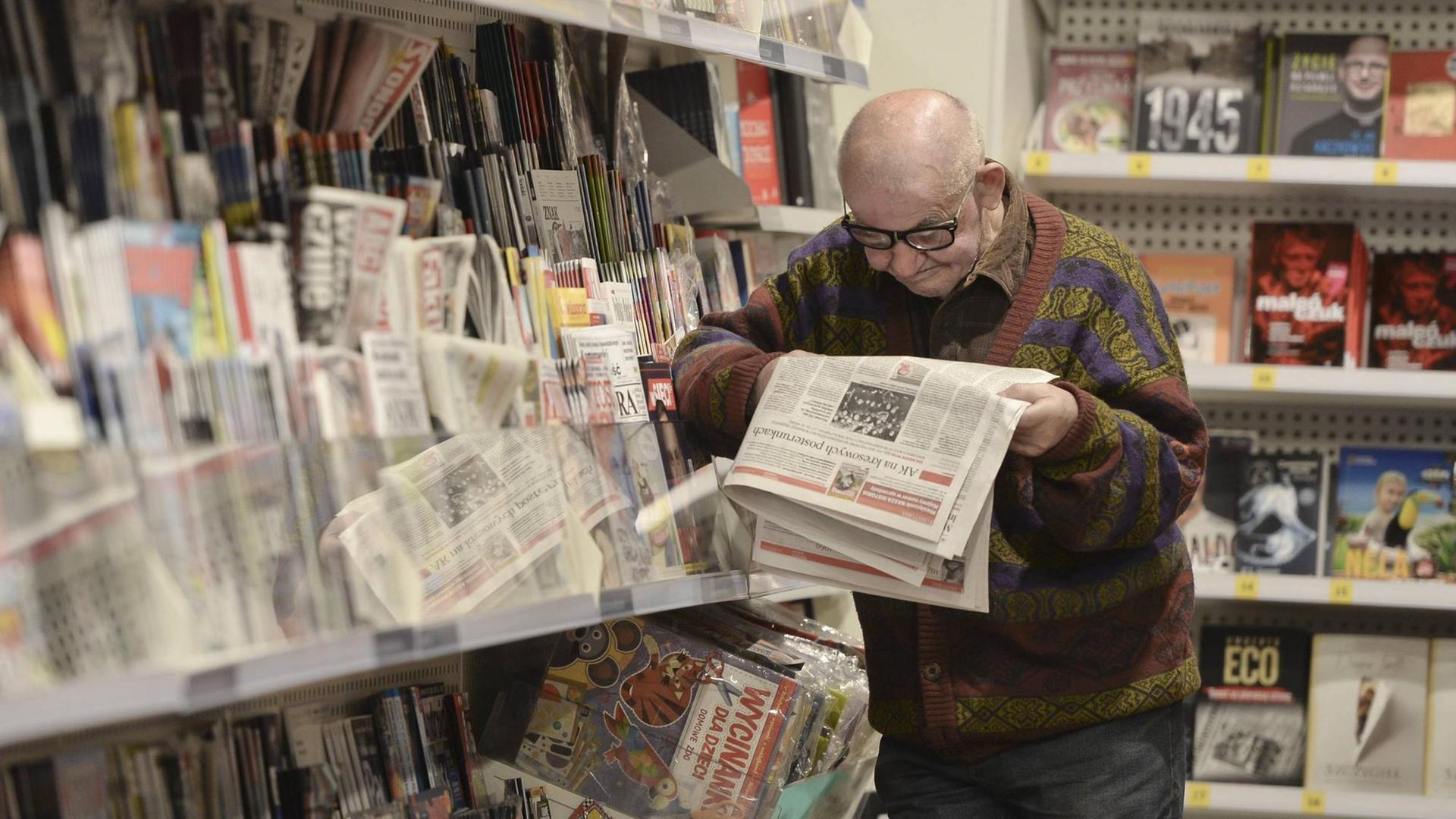 Mann lehnt an Zeitungsregal und liest in einer Zeitung Mann lehnt an Zeitungsregal und liest in einer Zeitung