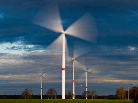 Schnell drehen sich die Rotoren von Windenergieanlagen auf einem Feld nahe Trampe in Brandenburg.