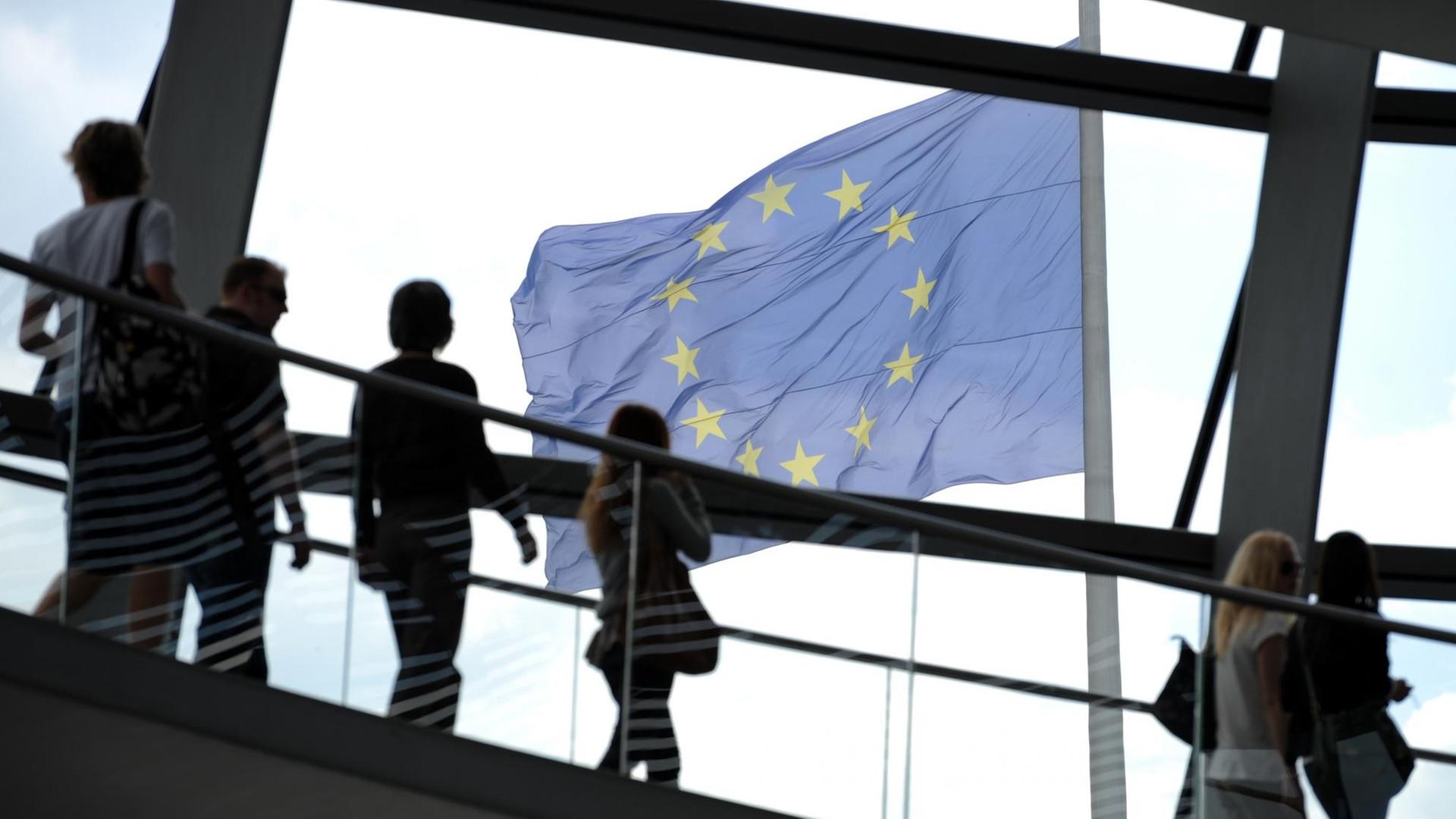 Ein Blick fällt durch die Besucher der Berliner Reichstagskuppel und durch die Scheiben des Gebäudes auf eine Europafahne, die auf dem Dach des Gebäudes befestigt ist und im Wind flattert. Ein Blick fällt durch die Besucher der Berliner Reichstagskuppel und durch die Scheiben des Gebäudes auf eine Europafahne, die auf dem Dach des Gebäudes befestigt ist und im Wind flattert.