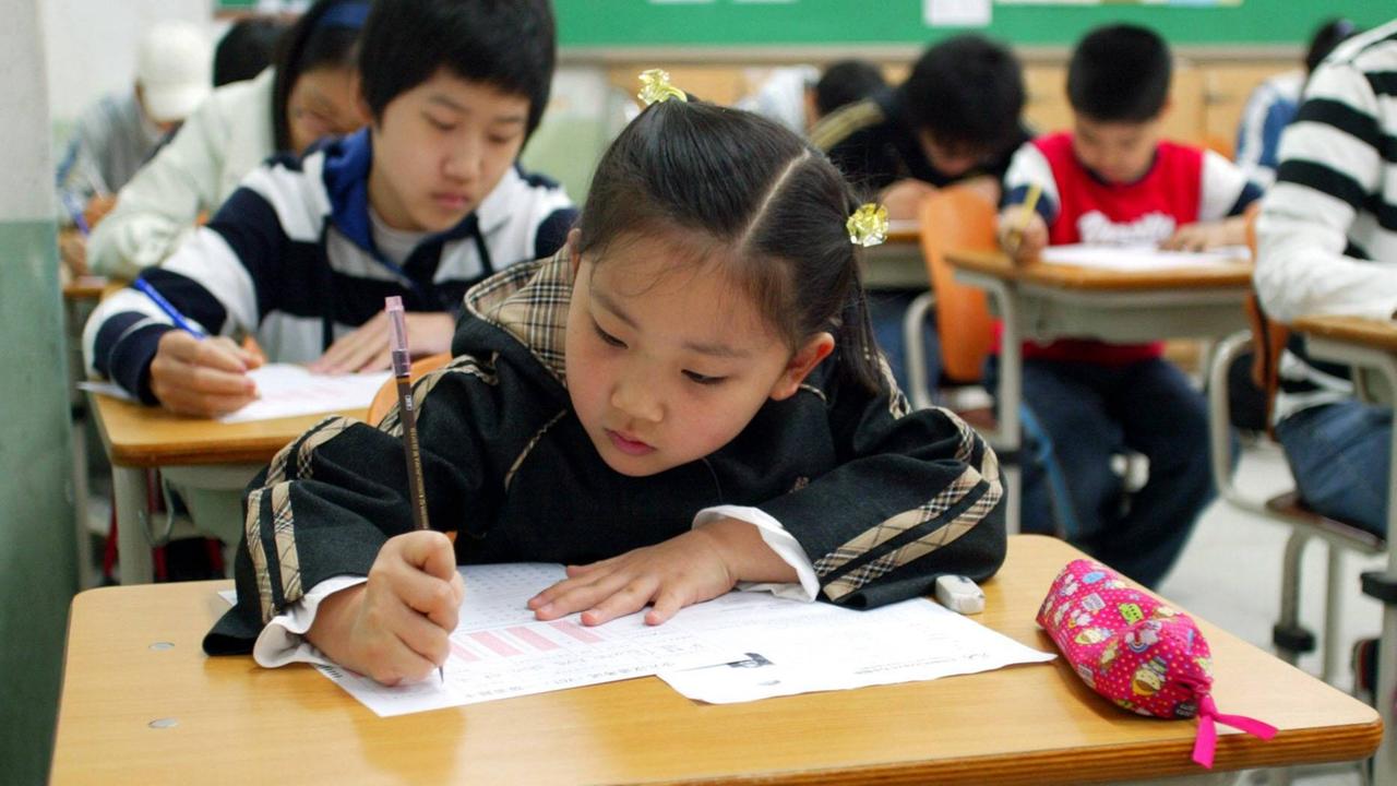 Eine Schulklasse in Südkorea, im Vordergrund beugt sich ein ca. zehnjähriges Mädchen über ein Papier und schreibt voller Ernst. Eine Schulklasse in Südkorea, im Vordergrund beugt sich ein ca. zehnjähriges Mädchen über ein Papier und schreibt voller Ernst.