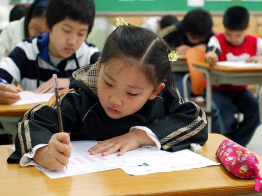 Eine Schulklasse in Südkorea, im Vordergrund beugt sich ein ca. zehnjähriges Mädchen über ein Papier und schreibt voller Ernst.