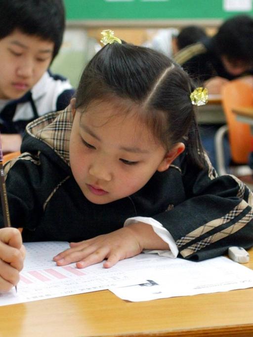 Eine Schulklasse in Südkorea, im Vordergrund beugt sich ein ca. zehnjähriges Mädchen über ein Papier und schreibt voller Ernst.