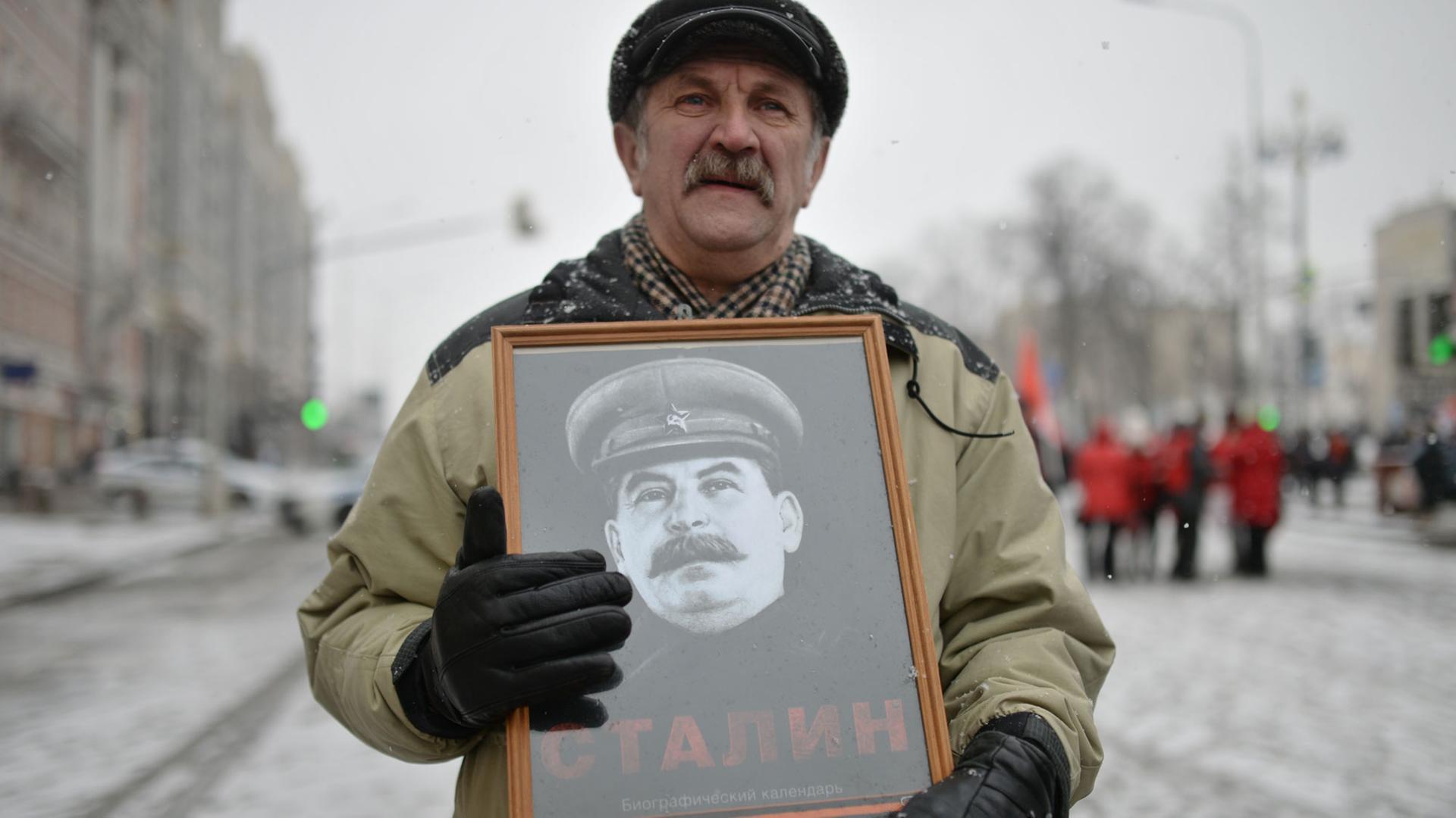 Ein Teilnehmer einer Prozession anlässlich des 99. Jahrestages der Entstehung der Sowjetarmee und der Marine hält ein gerahmtes Stalin-Bild in seinen Händen. Ein Teilnehmer einer Prozession anlässlich des 99. Jahrestages der Entstehung der Sowjetarmee und der Marine hält ein gerahmtes Stalin-Bild in seinen Händen.