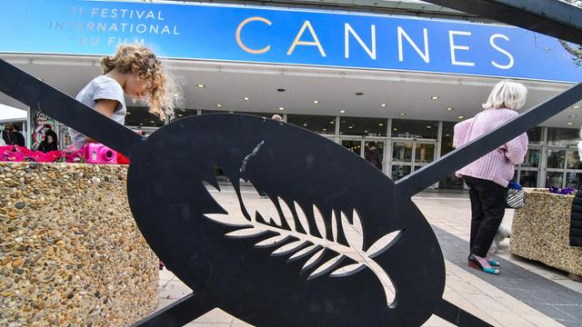 Ein Palmenblatt ist im Geländer vor einem Gebäude zu sehen, auf dem für die Filmfestspiele in Cannes geworben wird.
