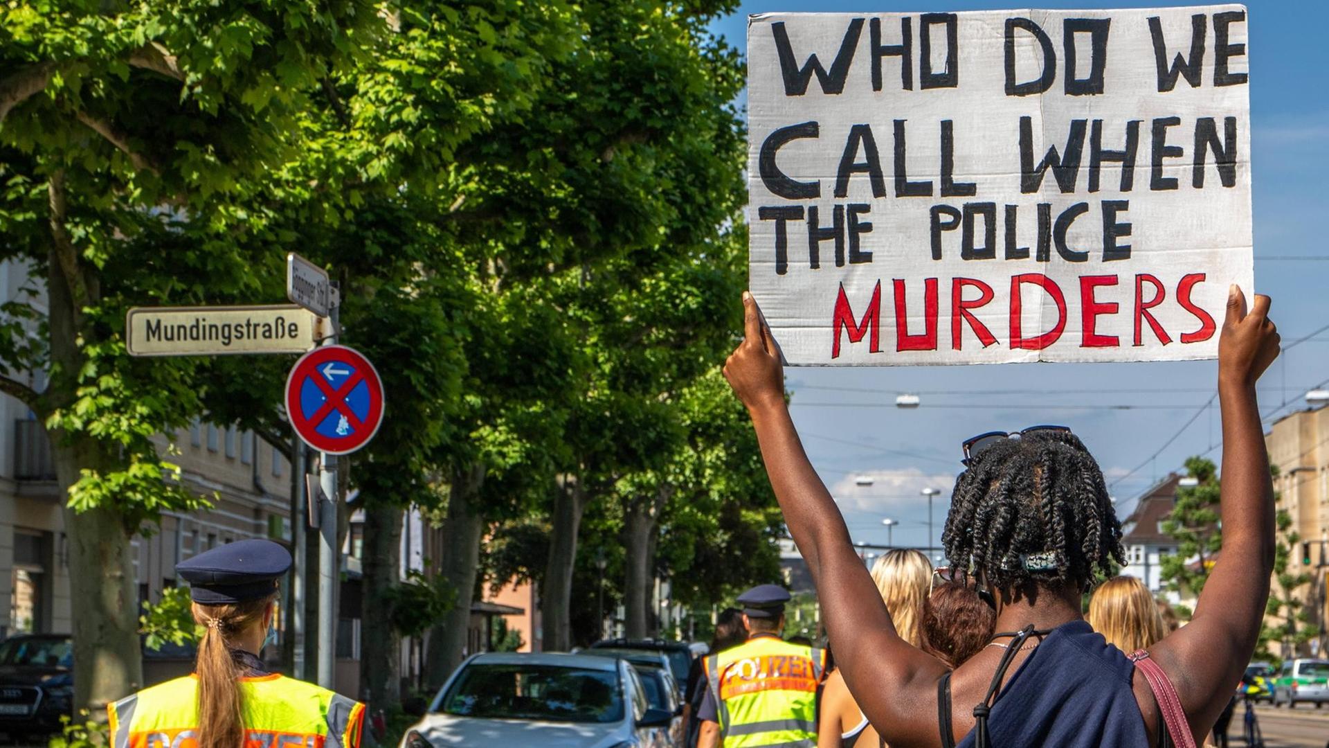 Bei einer Demo gegen Rassismus in Augsburg hält ein Mann ein Schild mit der Aufschrift "Who do we call when the police murders)" ("Wen rufen wir an, wenn die Polizei mordet?") hoch.
