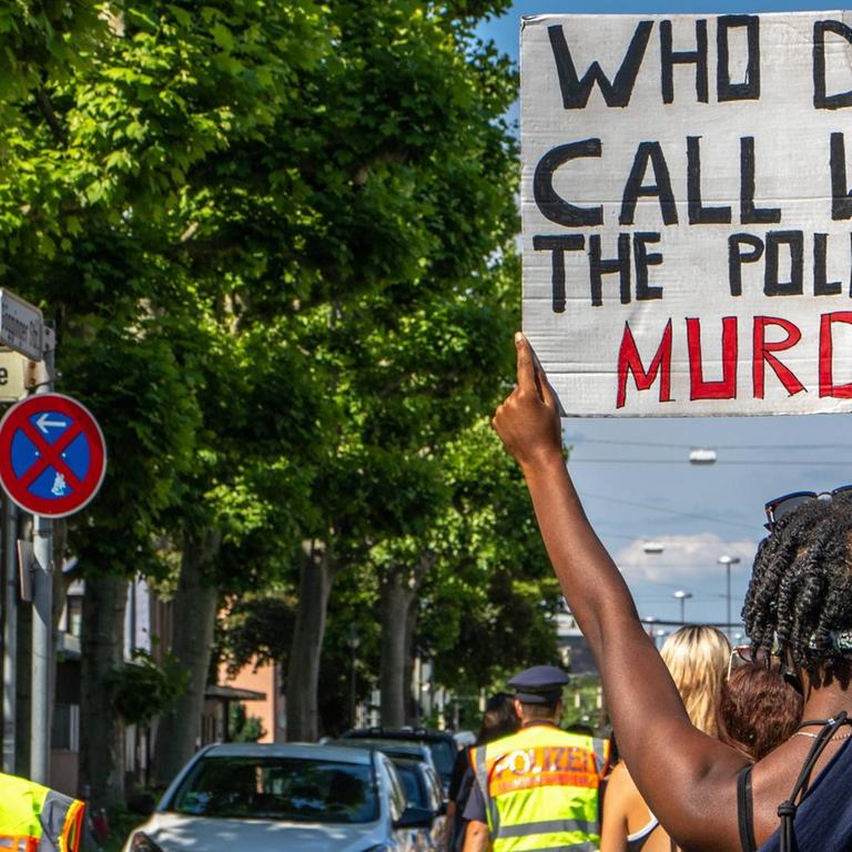 Bei einer Demo gegen Rassismus in Augsburg hält ein Mann ein Schild mit der Aufschrift "Who do we call when the police murders)" ("Wen rufen wir an, wenn die Polizei mordet?") hoch.
