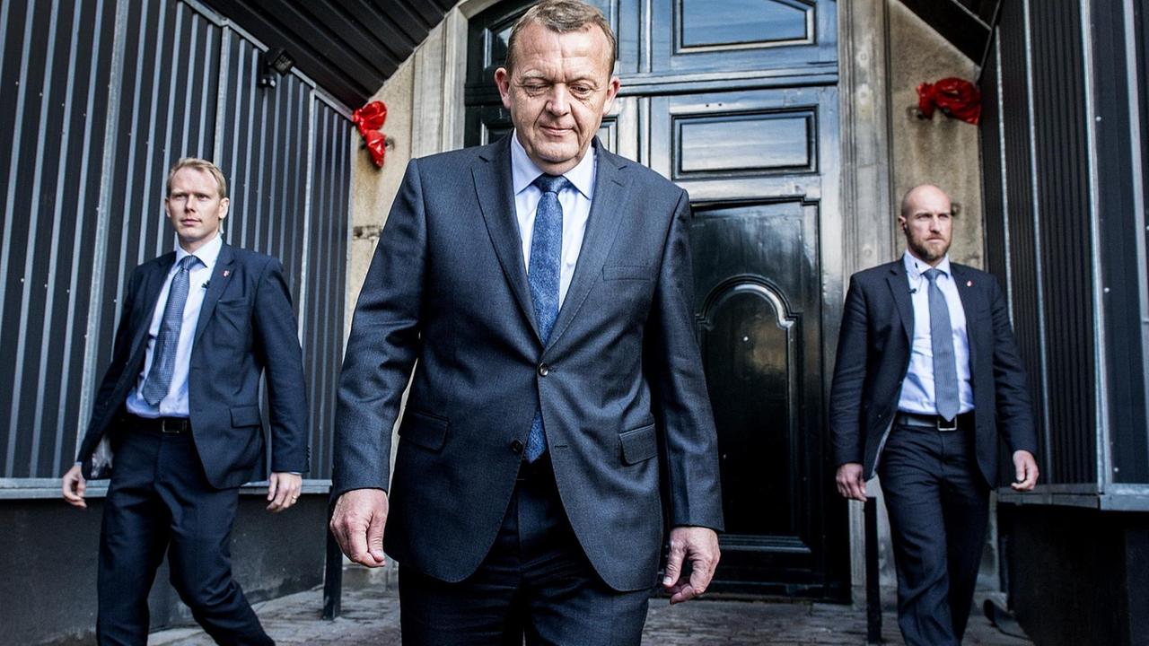 Rasmussen entfernt sich im schwarzen Anzug von einer Tür, rechts und links neben ihm laufen zwei Personenschützer. Rasmussen entfernt sich im schwarzen Anzug von einer Tür, rechts und links neben ihm laufen zwei Personenschützer.