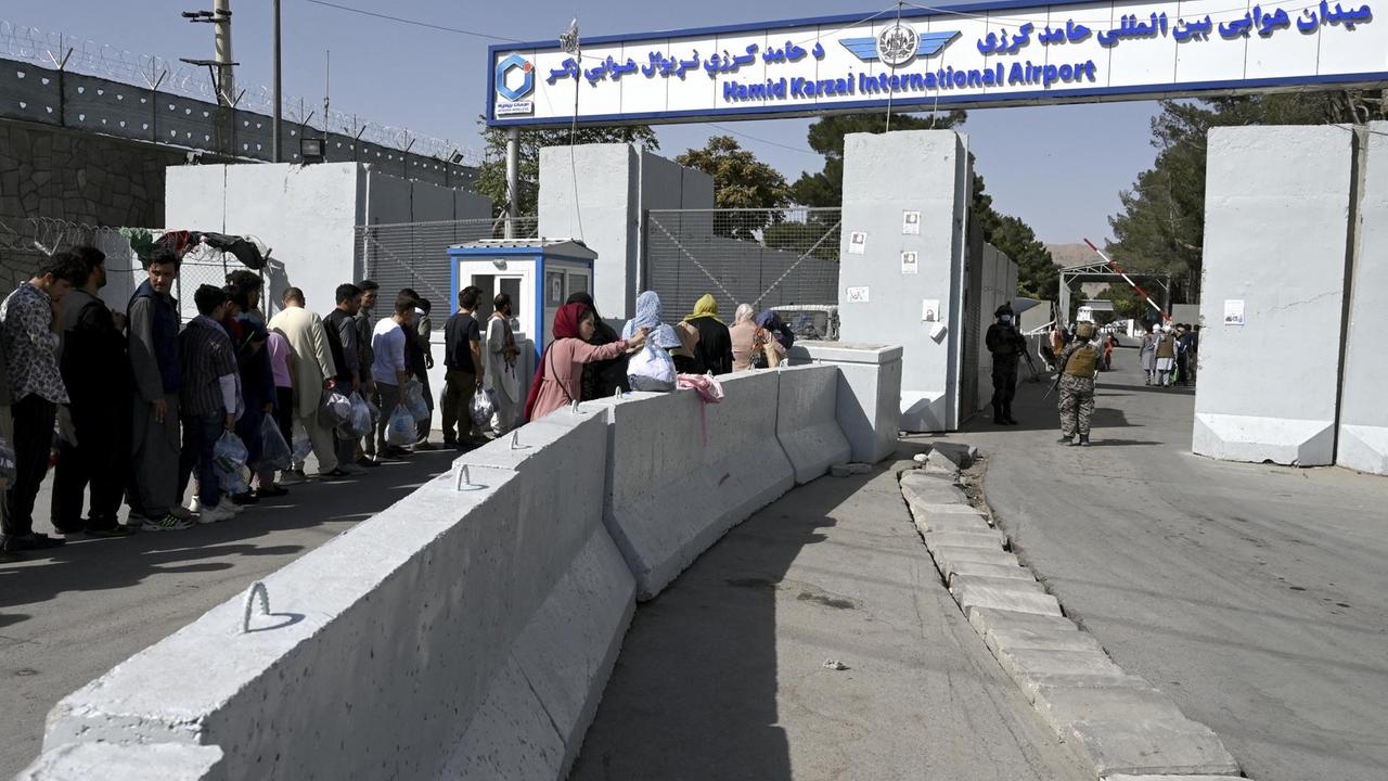 Menschen stehen in einer Schlange vor dem Haupteingang des Kabuler Flughafens. Auf einem Schild steht "Hamid Karzai International Airport". Menschen stehen in einer Schlange vor dem Haupteingang des Kabuler Flughafens. Auf einem Schild steht "Hamid Karzai International Airport".