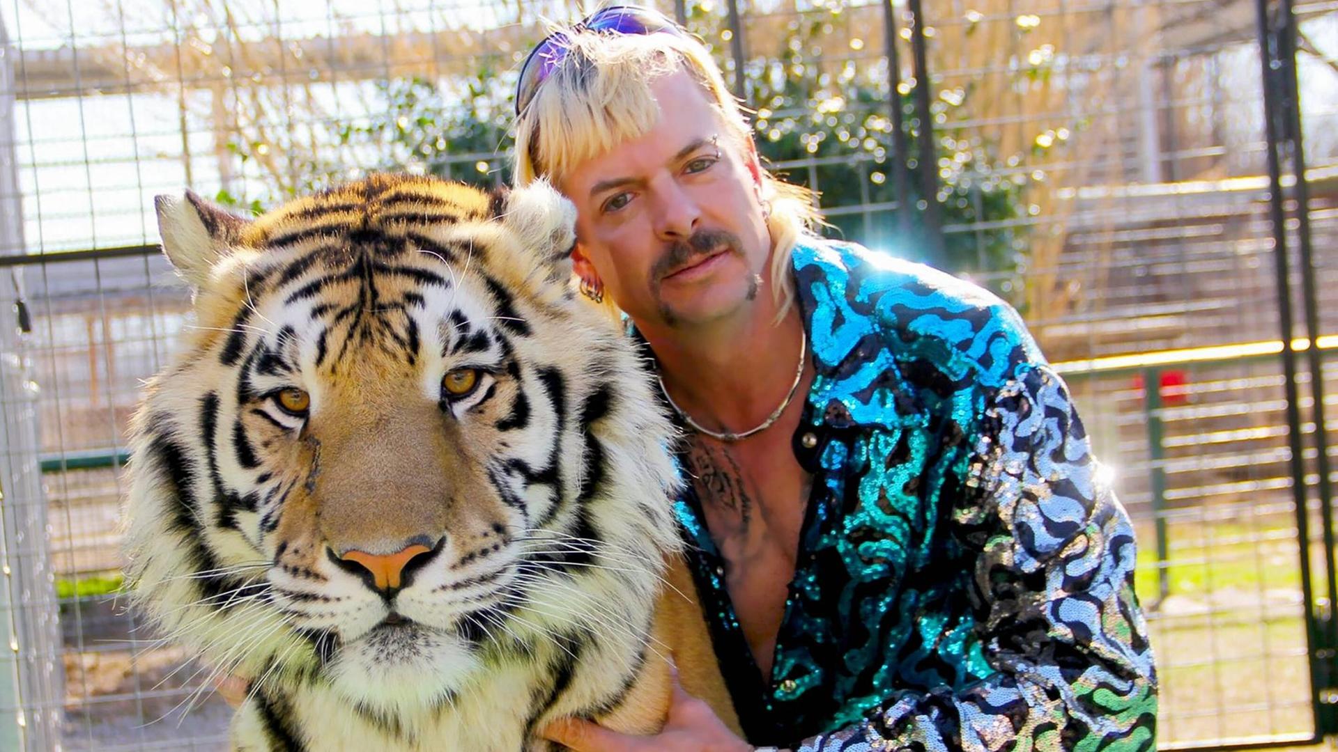 Ein Mann mit blonden Haaren und Schnauzbart kniet neben einem Tiger. Ein Mann mit blonden Haaren und Schnauzbart kniet neben einem Tiger.