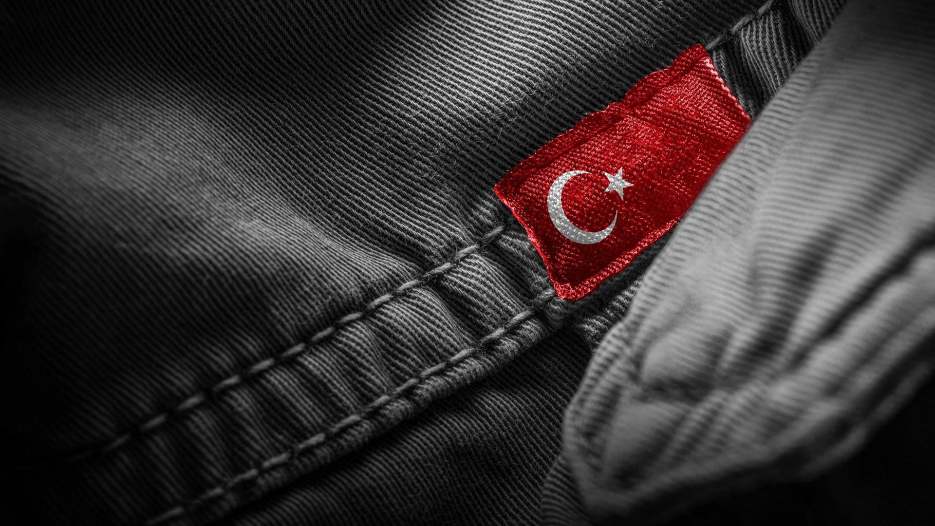 Eine türkische Flagge ist als Label auf ein dunkles Kleidungsstück genäht. Eine türkische Flagge ist als Label auf ein dunkles Kleidungsstück genäht.