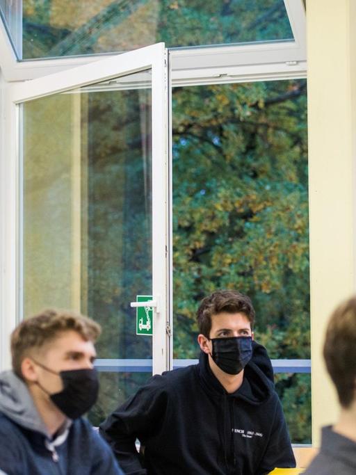 Schüler einer 13. Klasse der Oberstufe sitzen mit Masken im Deutsch-Unterricht vor einem geöffneten Fenster.