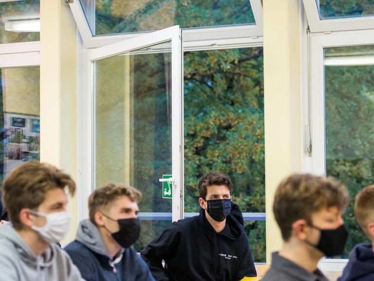 Schüler einer 13. Klasse der Oberstufe sitzen mit Masken im Deutsch-Unterricht vor einem geöffneten Fenster.