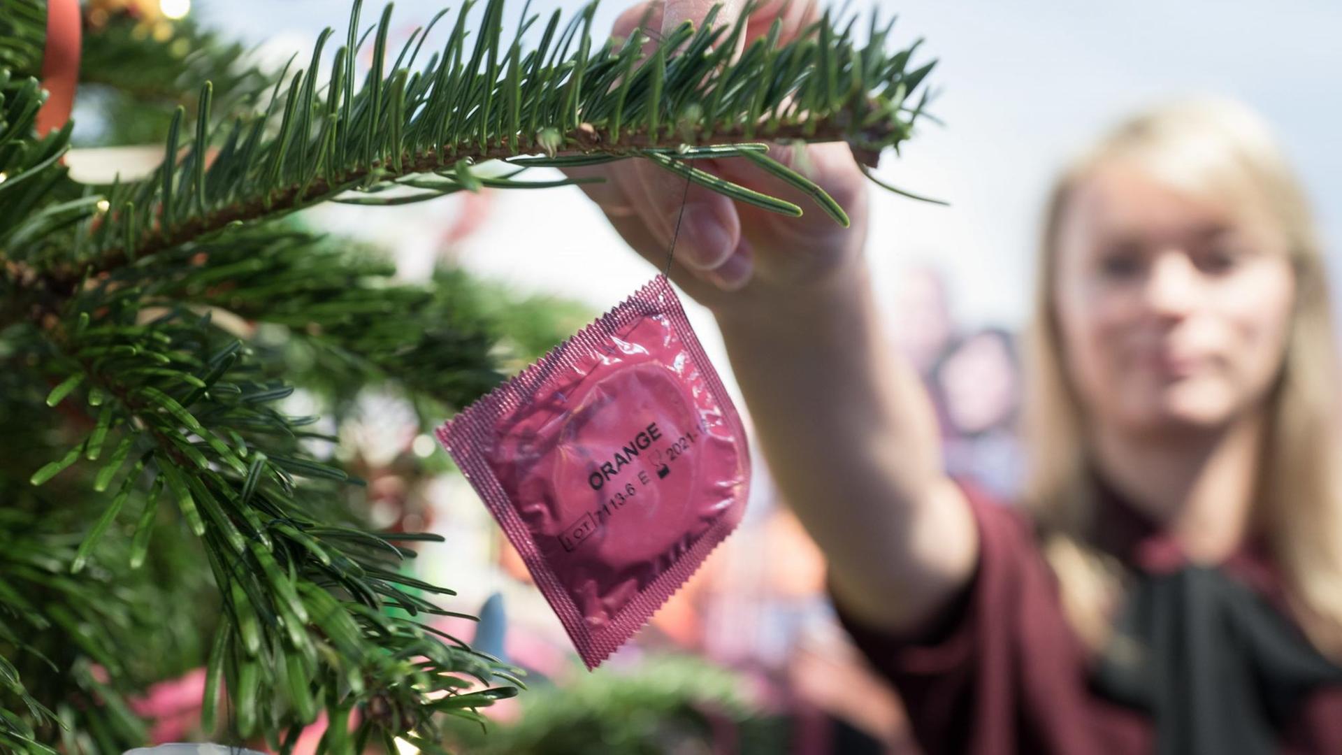 Eine Frau dekoriert einen Weihnachtsbaum mit einem Kondom. Eine Frau dekoriert einen Weihnachtsbaum mit einem Kondom.
