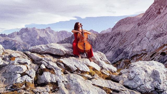 Raphaela Gromes sitzt mit ihrem Cello auf einem Felsen. Im Hintergrund ist ein Bergpanorama zu sehen