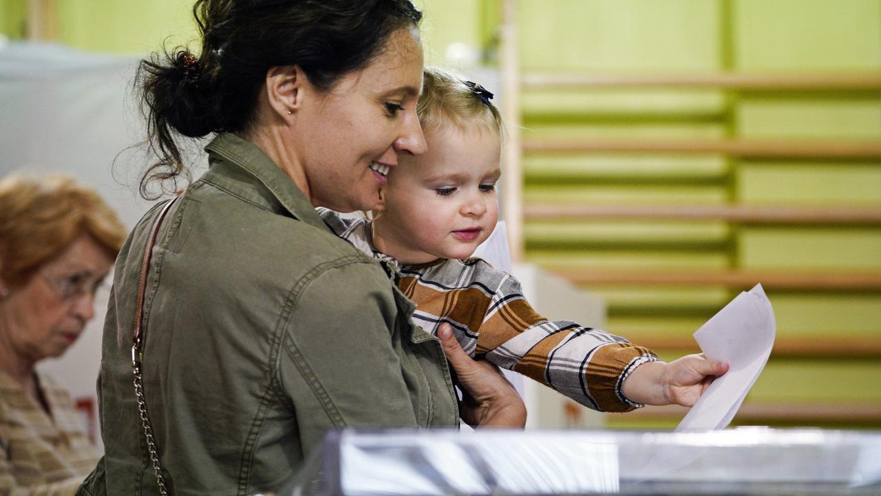 Eine junge Frau mit Kind auf dem Arm steht in Warschau an einer Wahlurne.