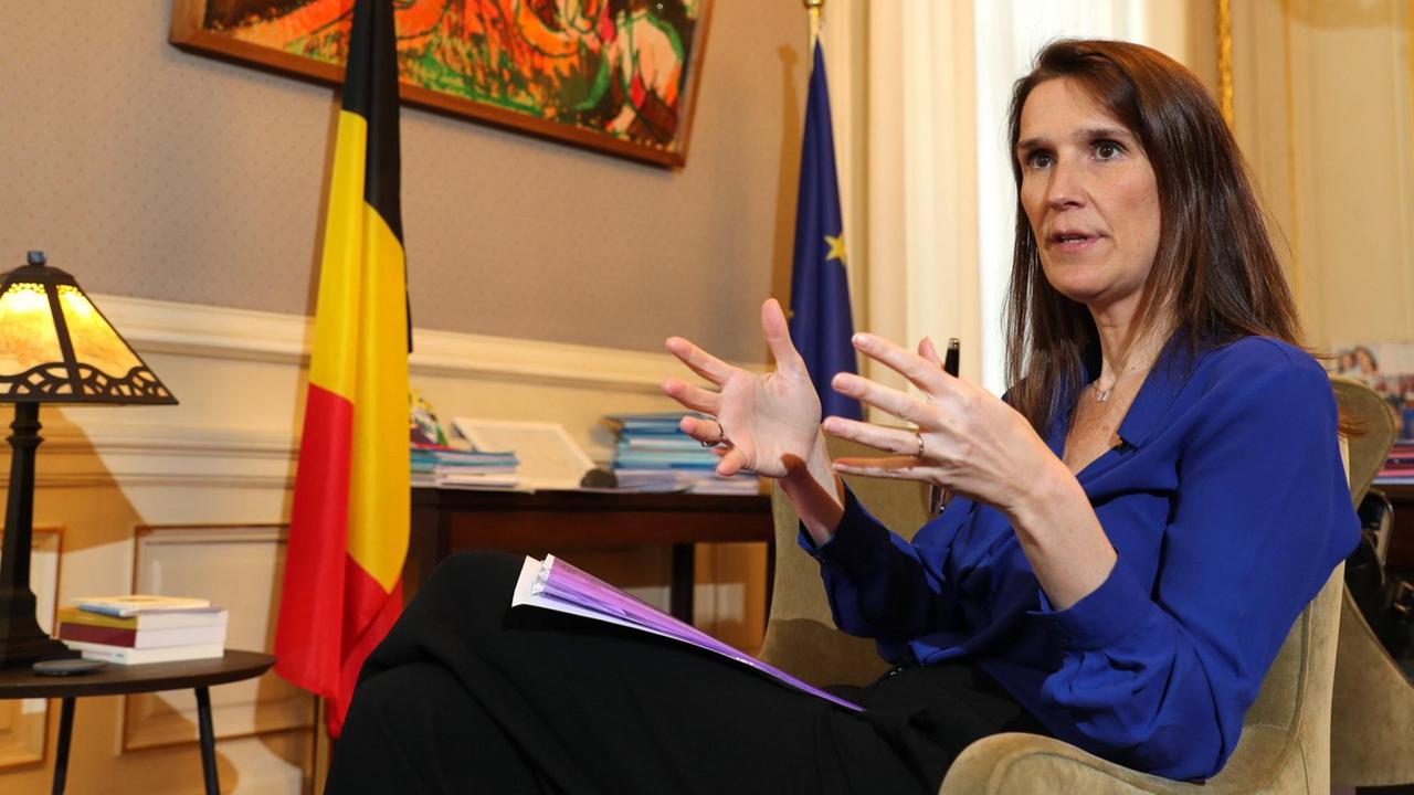 Sophie Wilmes sitzt ernst gestikulierend in einem repräsentativen, mit der Fahne Belgiens geschmückten Raum. Sophie Wilmes sitzt ernst gestikulierend in einem repräsentativen, mit der Fahne Belgiens geschmückten Raum.