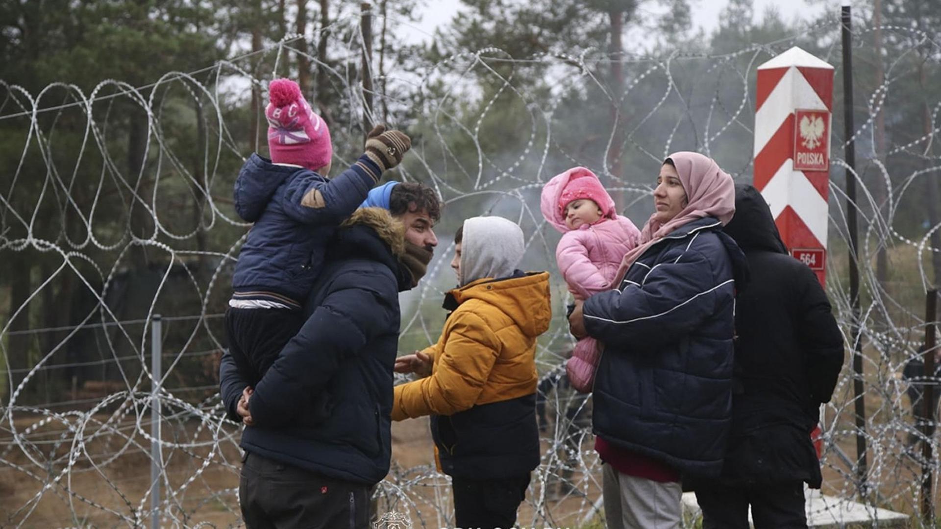 Belarus, Grodno: Auf diesem vom Staatlichen Grenzkomitee Belarus veröffentlichten Foto stehen Migranten mit Kindern vor einem Grenzzaun aus Stacheldraht an der belarussisch-polnischen Grenze.