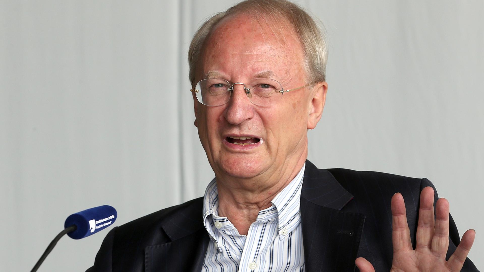 Klaus Staeck sitzt vor einem Mikrofon und hebt die Hand Klaus Staeck sitzt vor einem Mikrofon und hebt die Hand