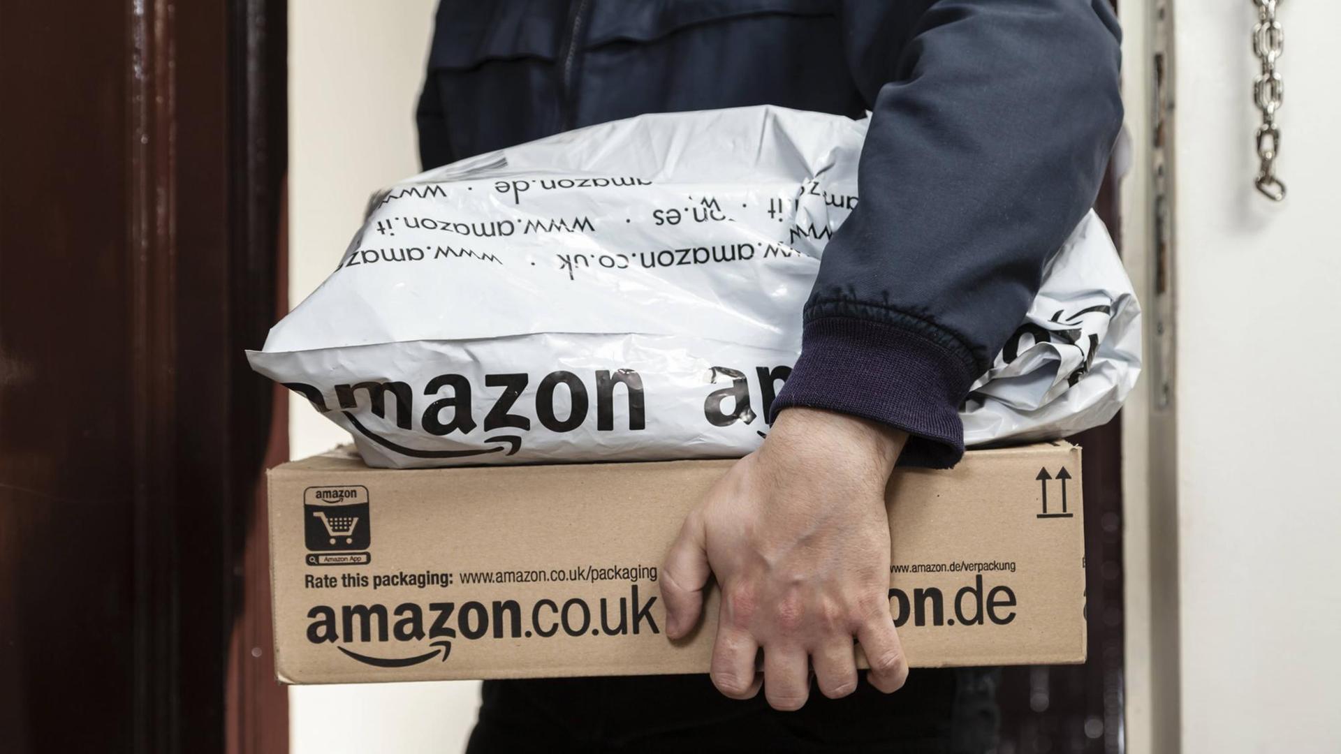 Ein Paketbote übergibt zwei Amazon-Pakete. Ein Paketbote übergibt zwei Amazon-Pakete.