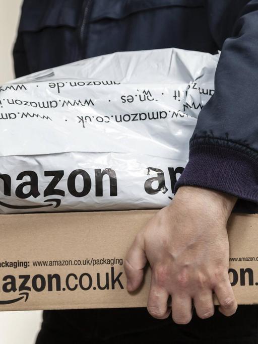 Ein Paketbote übergibt zwei Amazon-Pakete.