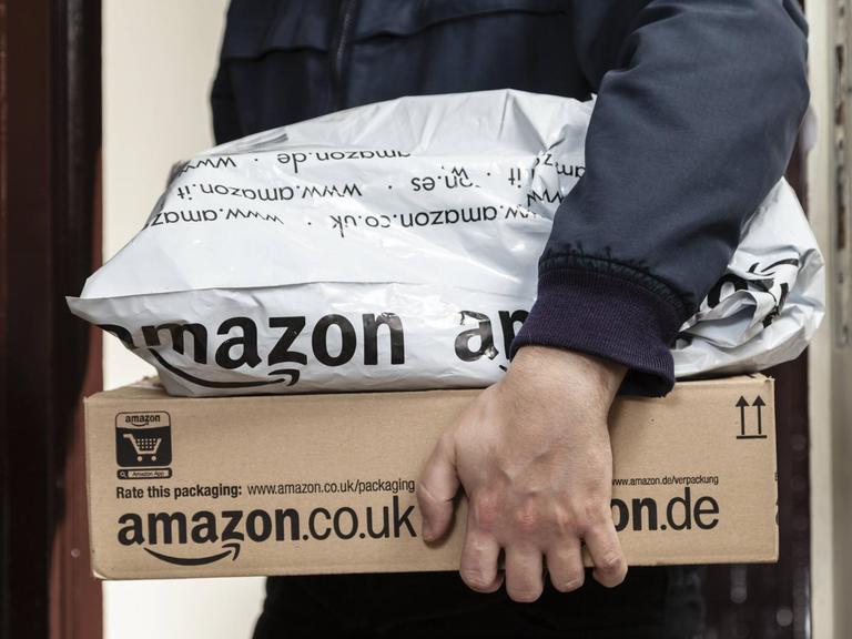 Ein Paketbote übergibt zwei Amazon-Pakete.
