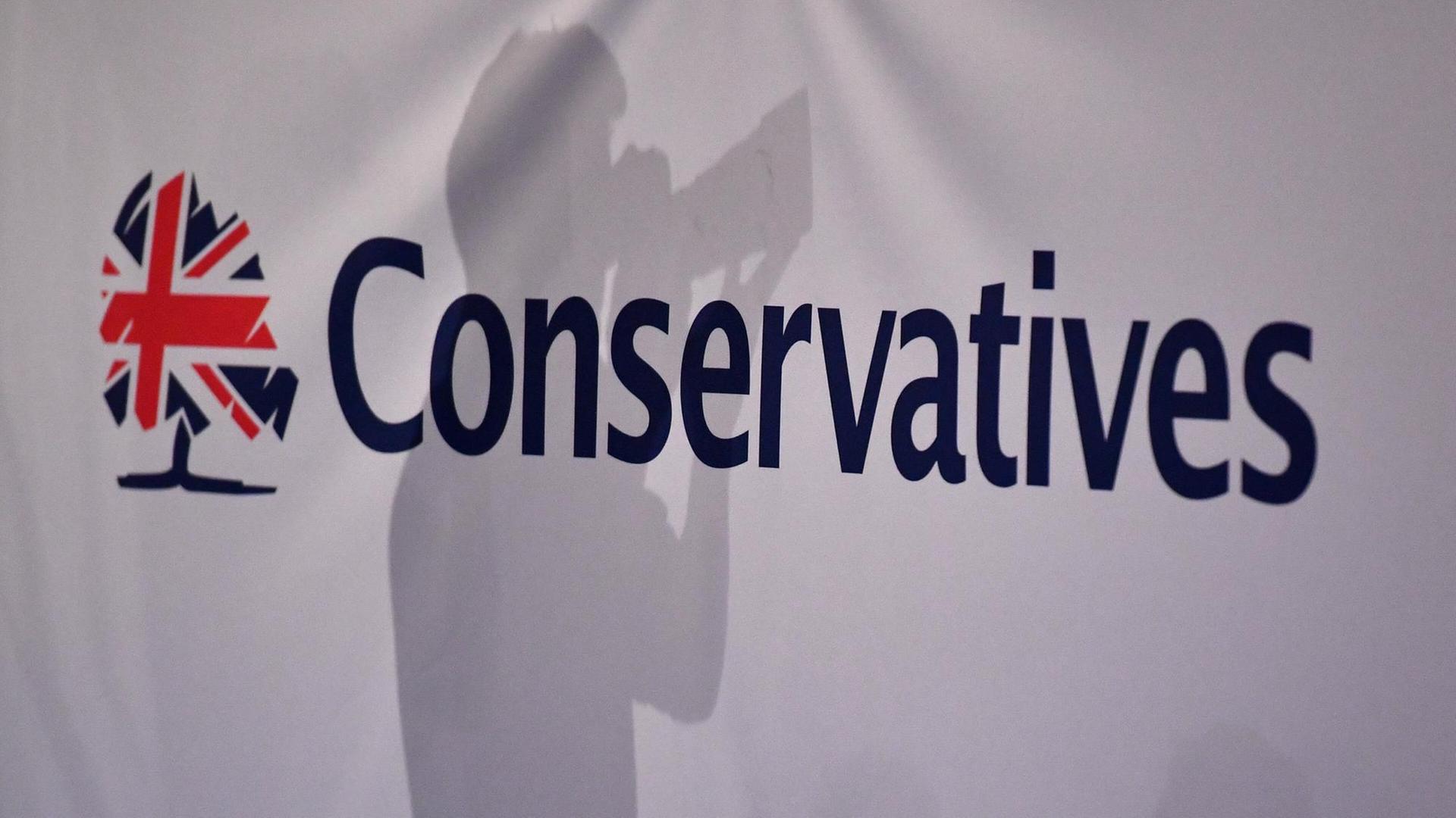 Der Schatten eines Pressefotografen ist vor dem Logo des Parteitags der Konservativen in Großbritannien zu sehen. Der Schatten eines Pressefotografen ist vor dem Logo des Parteitags der Konservativen in Großbritannien zu sehen.