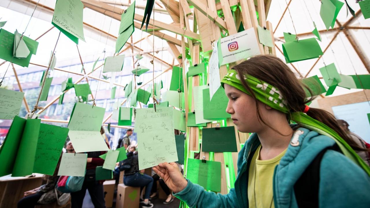 Eine junge Frau steht beim Evangelischen Kirchentag im Pavillon der Guten Nachricht und liest einen der vielen handgeschriebenen Zettel, die die Besucher dort aufhängen können. Eine junge Frau steht beim Evangelischen Kirchentag im Pavillon der Guten Nachricht und liest einen der vielen handgeschriebenen Zettel, die die Besucher dort aufhängen können.