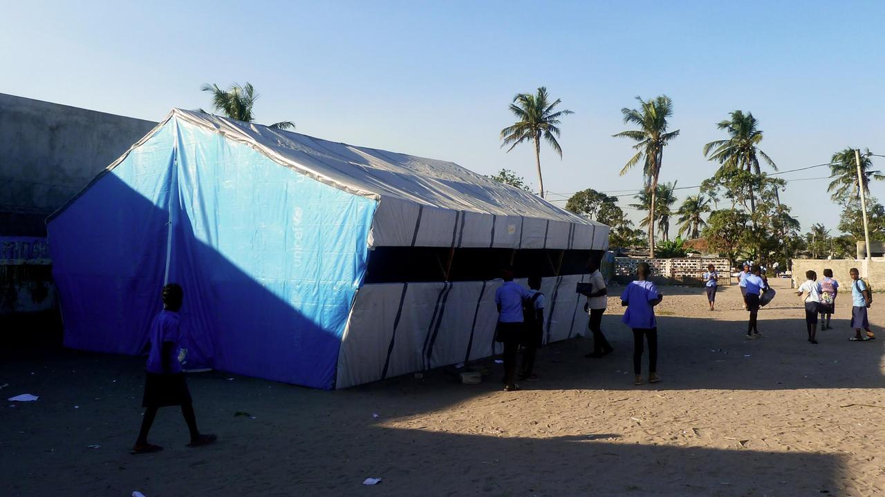 Vor einem blauweißen Zelt stehen Schüler und Schülerinnen in Schuluniformen.