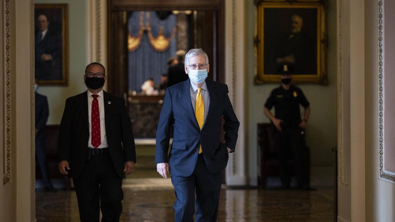 Mit Mundschutz, gelber Krawatte und blauem Anzug läuft ein Mann durch den Flur im Capitol in Washington.