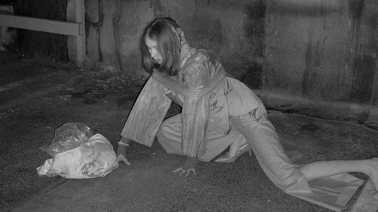 Eine Frau in aufwendiger Mode kriecht auf dem Boden eines Parkhauses
