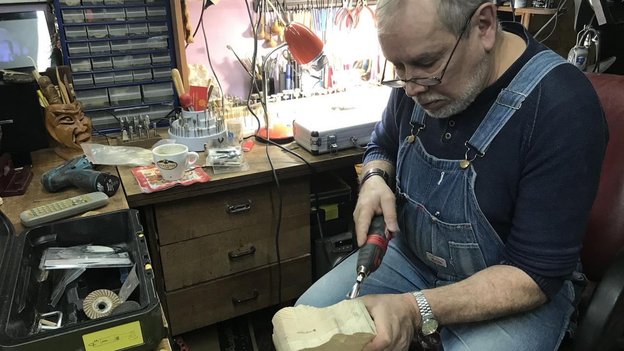 Ein Mann mittleren Alters schnitzt in seiner Werkstatt