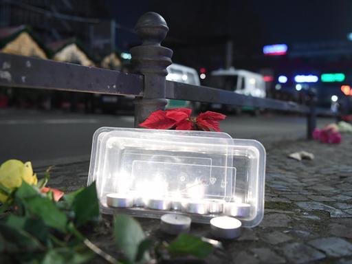 Blumen und Teelichter zum Gedenken an die Opfer stehen an einem Geländer vor dem Weihnachtsmarkt an der Gedächtniskirche in Berlin.