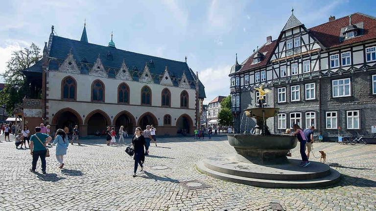 Passanten gehen in Goslar (Niedersachsen) auf dem Marktplatz am Marktbrunnen vorbei. Links ist das Goslarer Rathaus zu sehen. Passanten gehen in Goslar (Niedersachsen) auf dem Marktplatz am Marktbrunnen vorbei. Links ist das Goslarer Rathaus zu sehen.