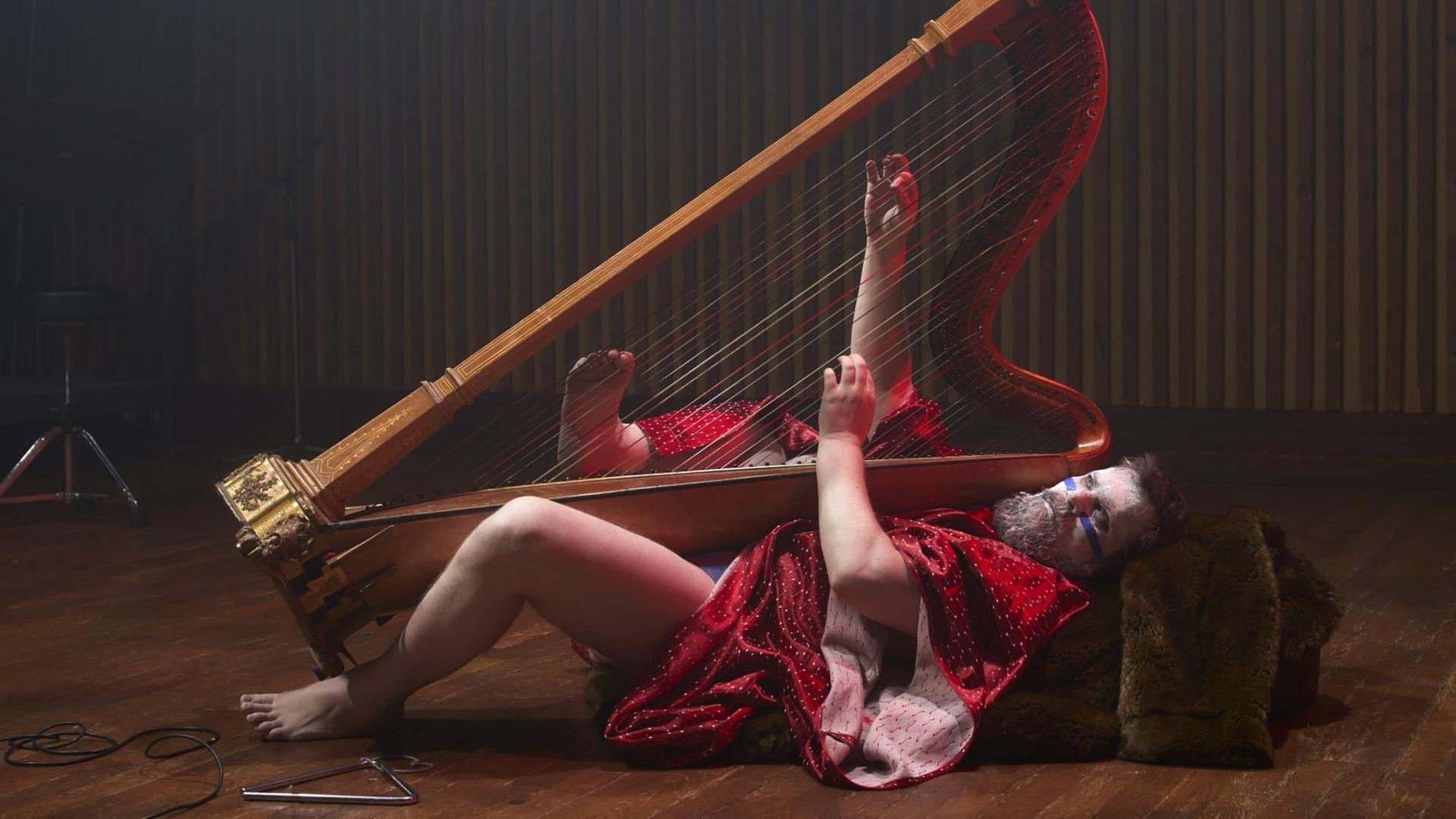 Musiker John Grant liegt kostümiert auf dem Rücken mit einer Harfe in den Händen