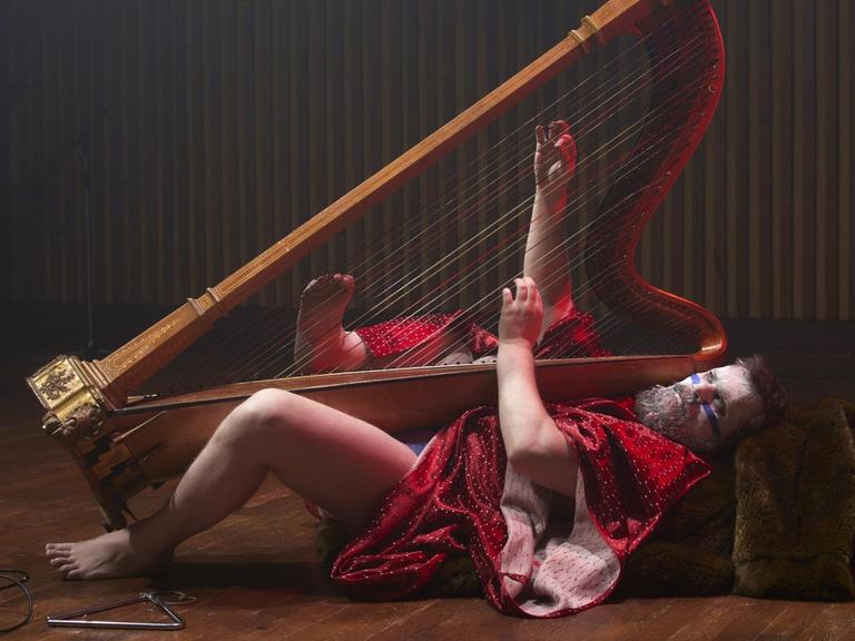 Musiker John Grant liegt kostümiert auf dem Rücken mit einer Harfe in den Händen
