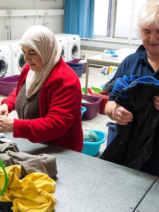 Eine Dame legt zusammen mit einer Flüchtlingsfrau Kleidung in einer Wäscherei zusammen.