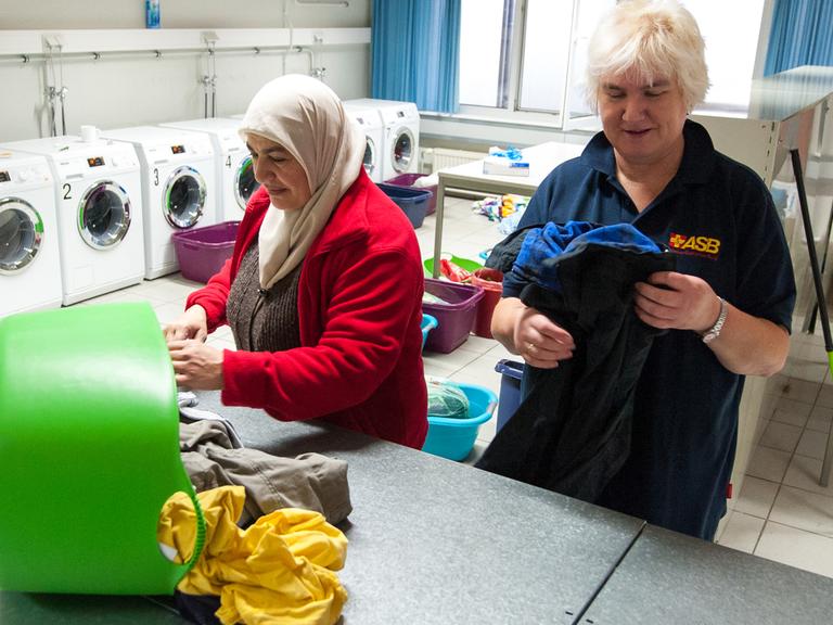 Eine Mitarbeiterin des Arbeiter-Samariter-Bundes legt zusammen mit einer Flüchtlingsfrau in Sumte Kleidung in der Wäscherei zusammen.