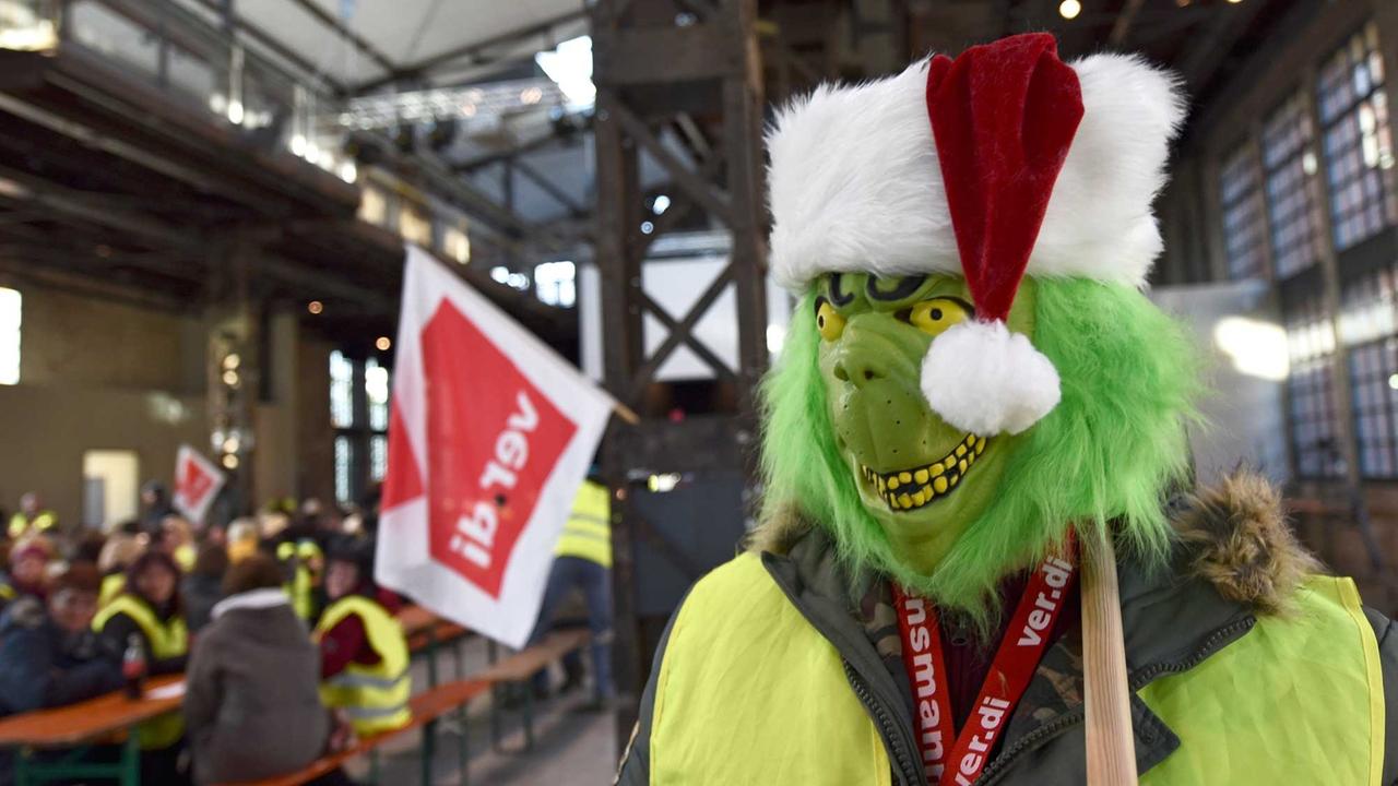 Verkleidet mit einer Grinch-Maske geht am 15.12.2014 ein Mann auf der Streikversammlung von Amazon-Mitarbeitern in Bad Hersfeld (Hessen) durch das Streiklokal.